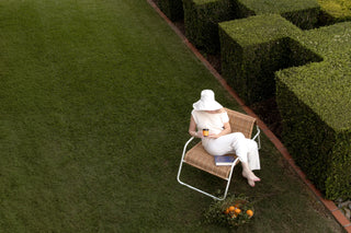 Person sitting on a chair in a garden with neatly trimmed hedges.